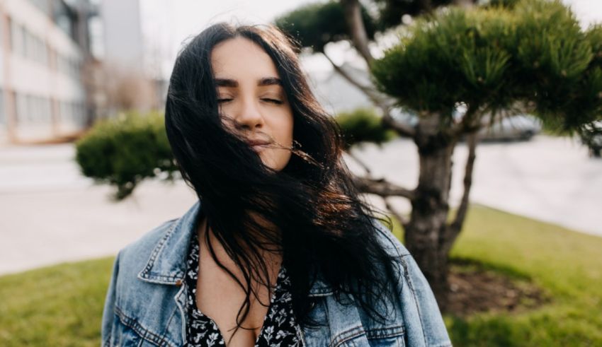 A young woman in a denim jacket standing in front of a tree.