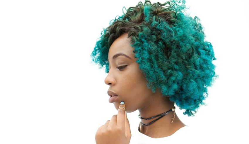 A woman with blue hair is putting her finger on her chin.