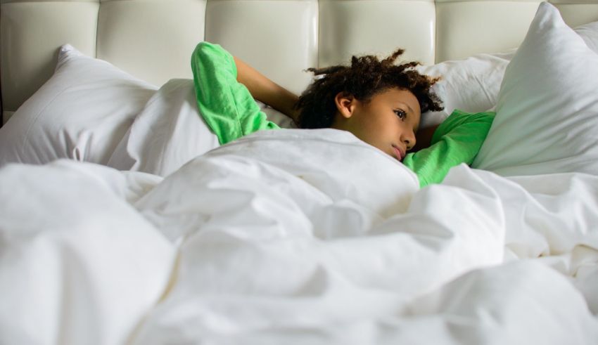 A young boy laying in bed with white sheets.