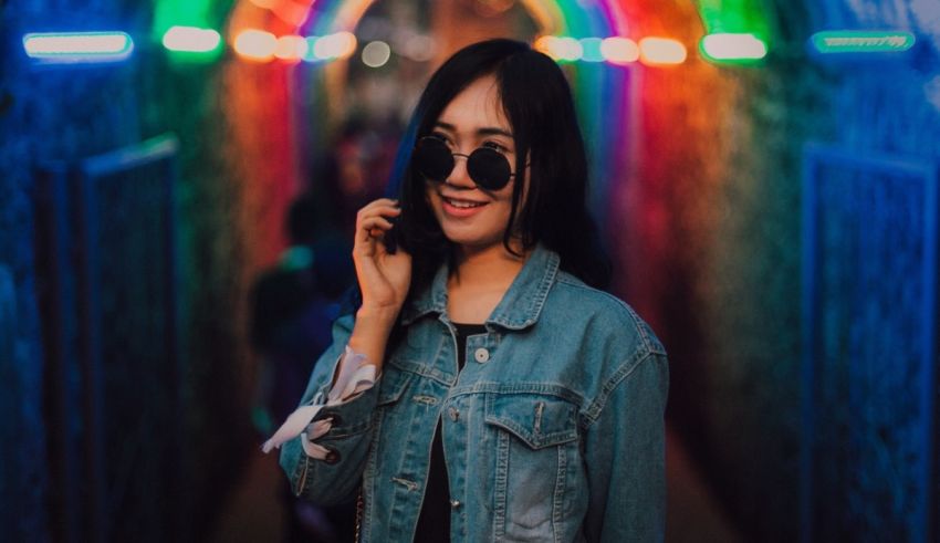 A young woman in a denim jacket standing in a tunnel with colorful lights.
