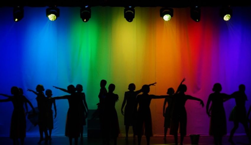 Silhouettes of dancers on stage with a rainbow colored backdrop.