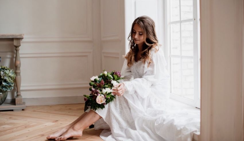 A woman in a white dress sits on the floor in front of a window.