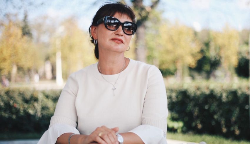 A woman in sunglasses sitting on a bench in a park.
