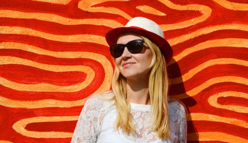 A woman wearing a hat and sunglasses in front of a red wall.