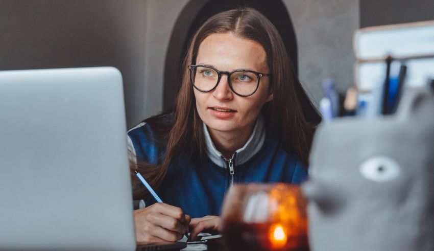 A woman wearing glasses is working on her laptop.