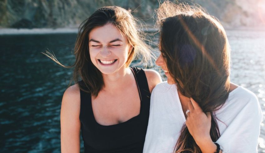 Two young women laughing in front of a body of water.