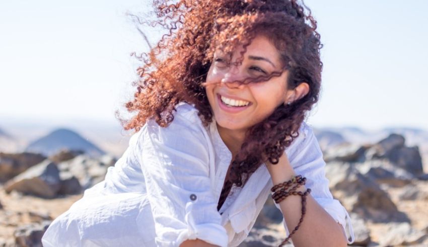 A woman with curly hair sitting on a rock in the desert.