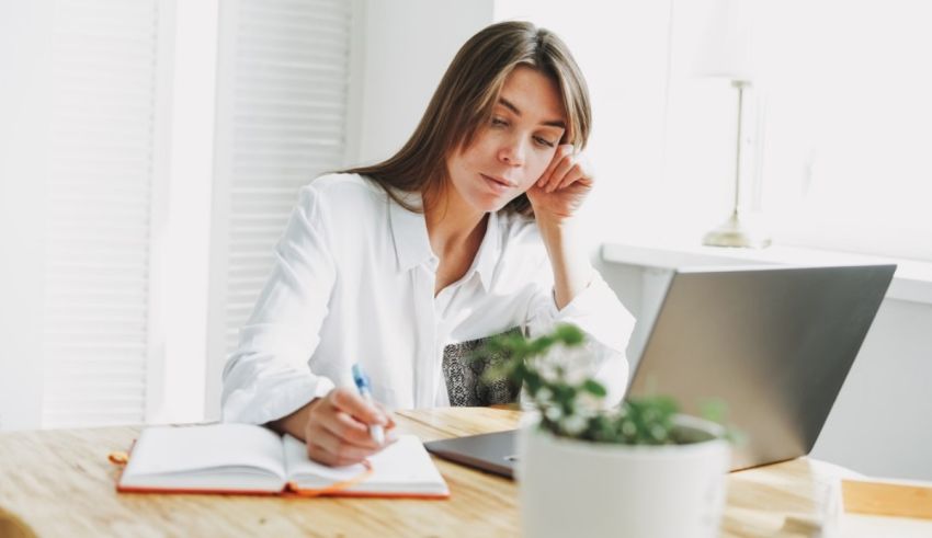 A woman is sitting at a table with a laptop and a notebook.