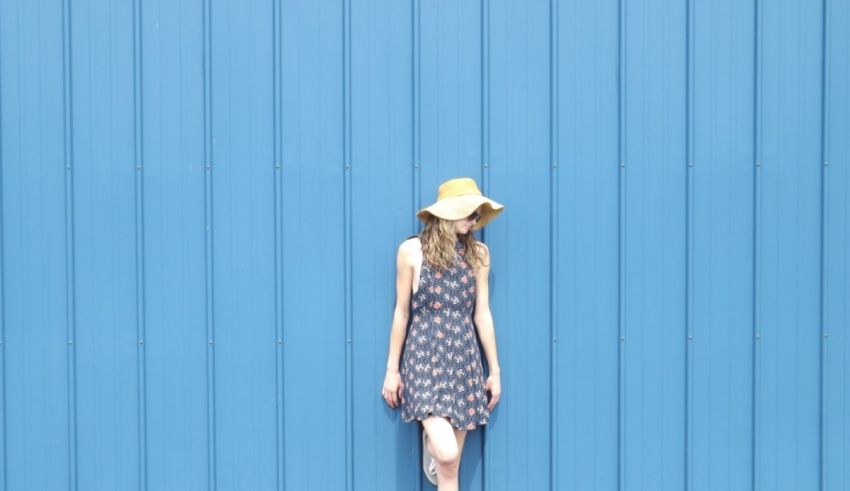 A woman leaning against a blue wall wearing a hat.