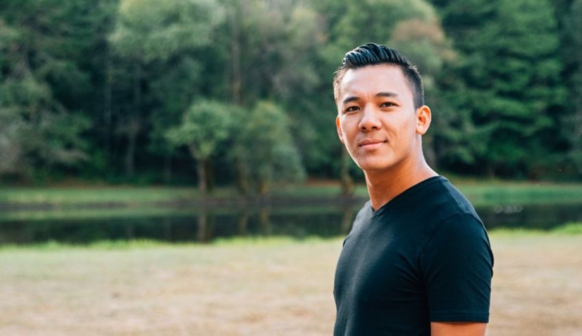 A man in a black shirt standing in front of a lake.