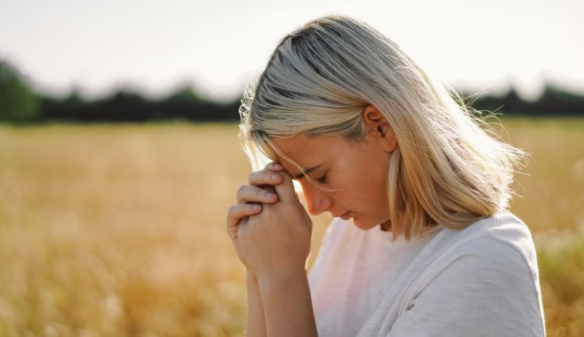 A young woman praying in a field.