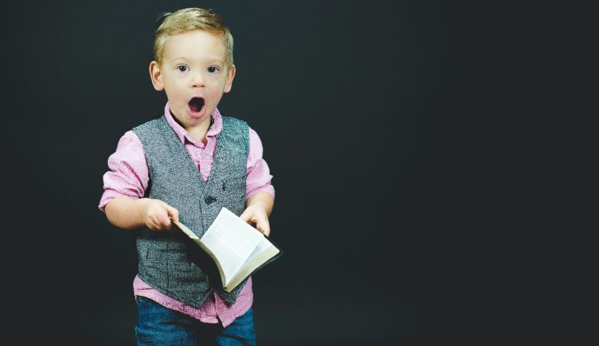 A young boy holding a book with his mouth open.