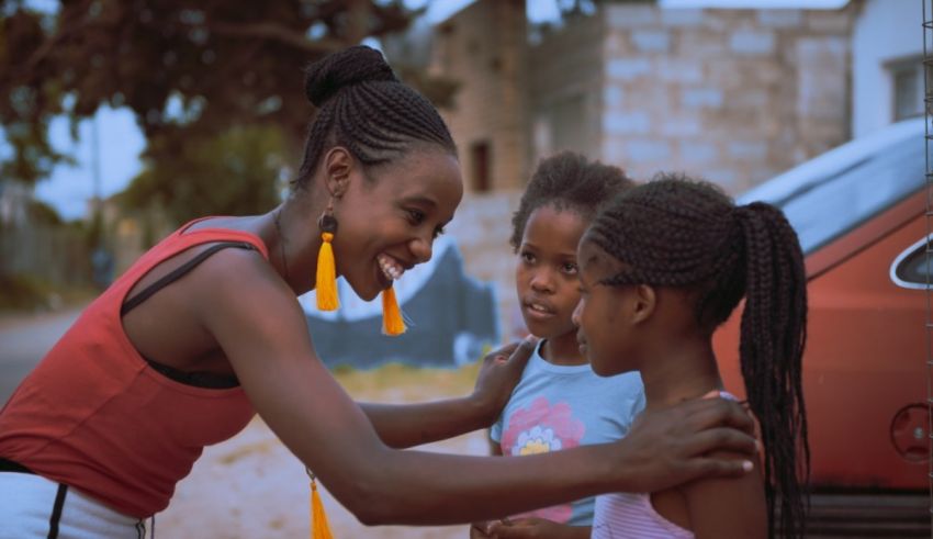 A woman is hugging two little girls in front of a car.