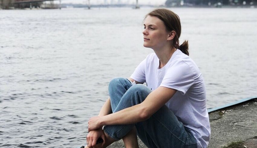 A woman sitting on the edge of a body of water.