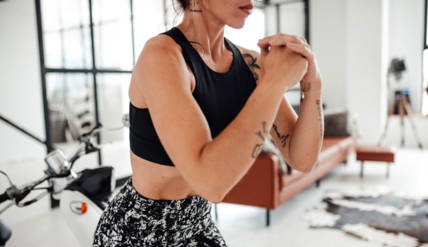 A woman in a black tank top and black leggings is working out in a living room.