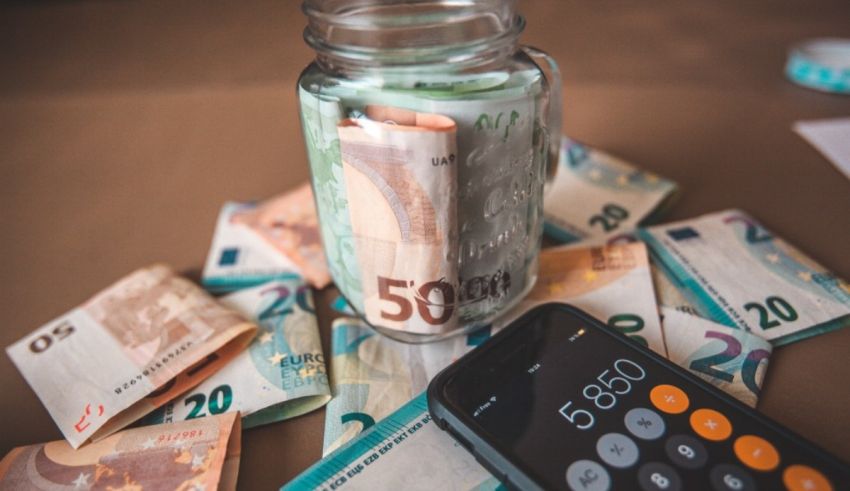 A jar full of money and a cell phone on a table.