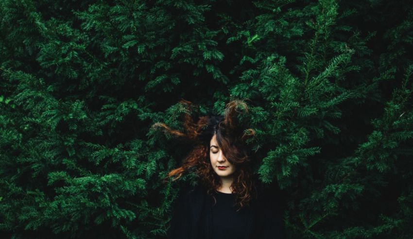 A woman with curly hair standing in front of a tree.