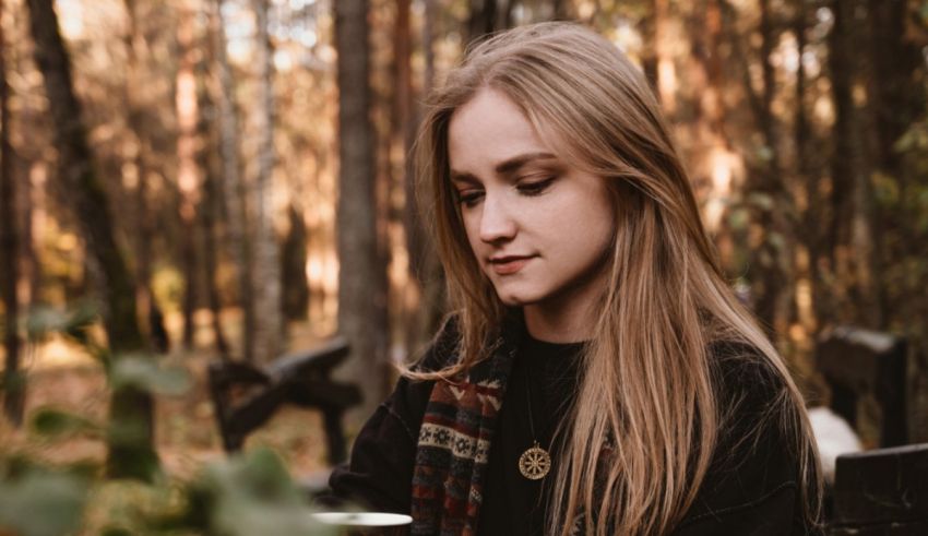 A girl sitting in the woods with a cup of coffee.