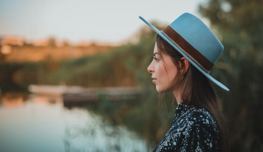 A young woman wearing a blue hat in front of a lake.