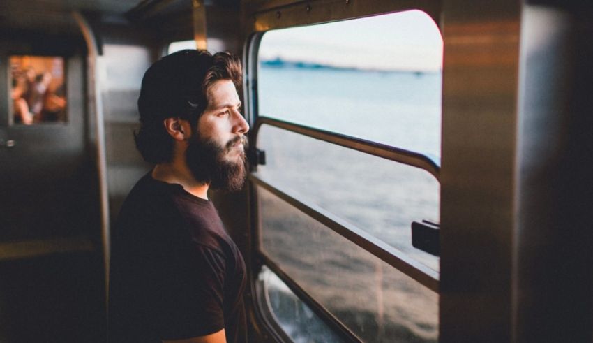A bearded man looking out the window of a train.