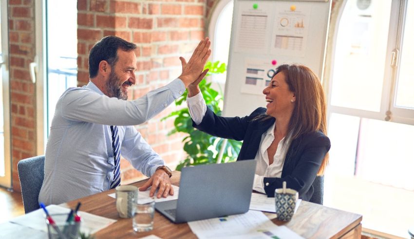 Two business people giving each other high fives in an office.