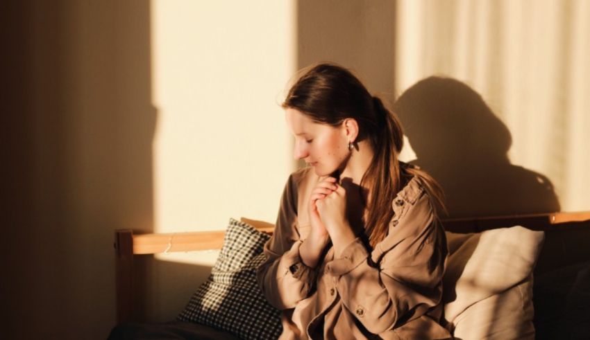 A woman is sitting on a bed in front of a window.