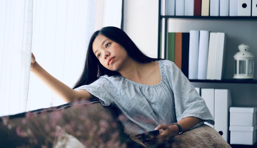 A young asian woman sitting on a couch looking out the window.