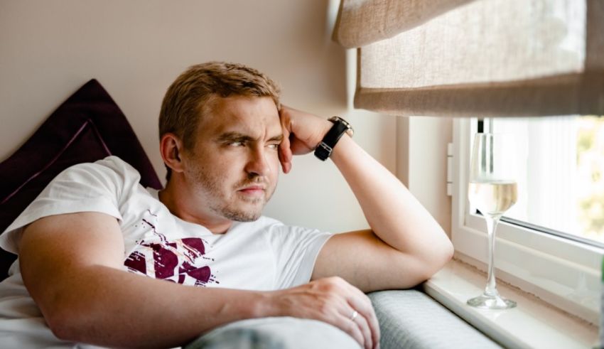 A man sitting on a window sill looking at a glass of wine.