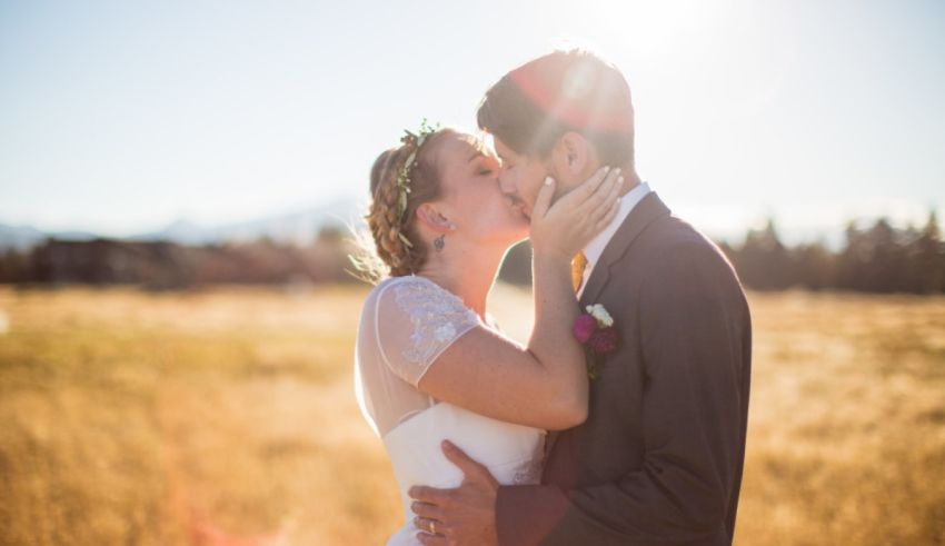 A bride and groom kissing in a field with mountains in the background.