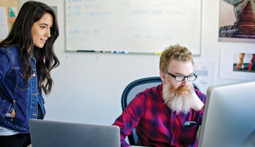 A man and woman working on a laptop in an office.