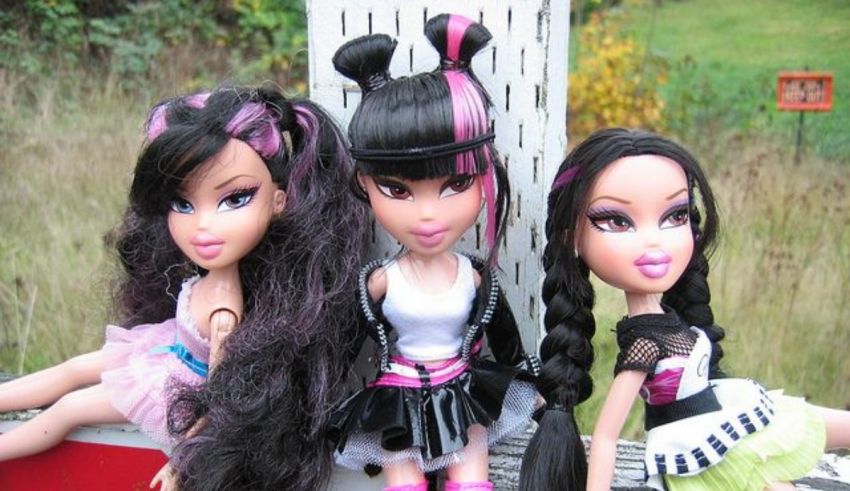 Three bratz dolls sitting on a bench.