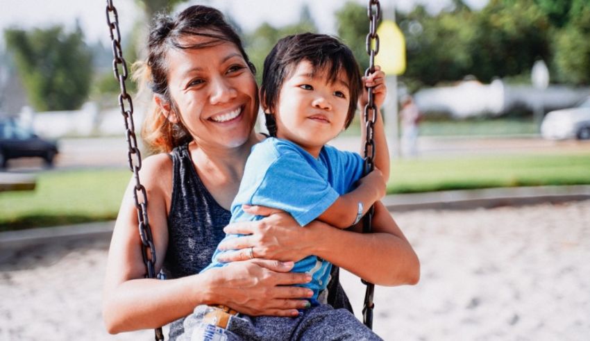 A woman holding a child on a swing in a park.