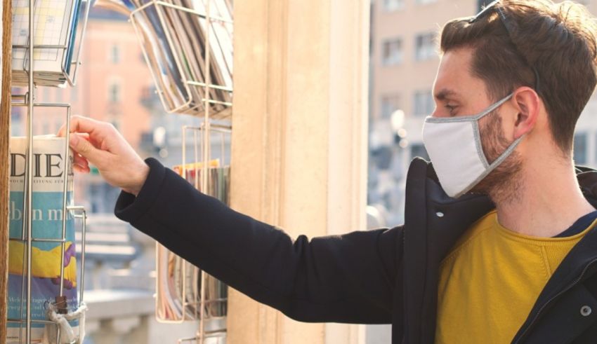 A man wearing a face mask looking at a newspaper.