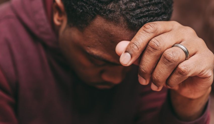 A black man is holding his head in his hands.