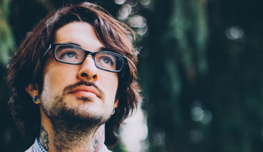 A man with glasses and tattoos looking up at the sky.