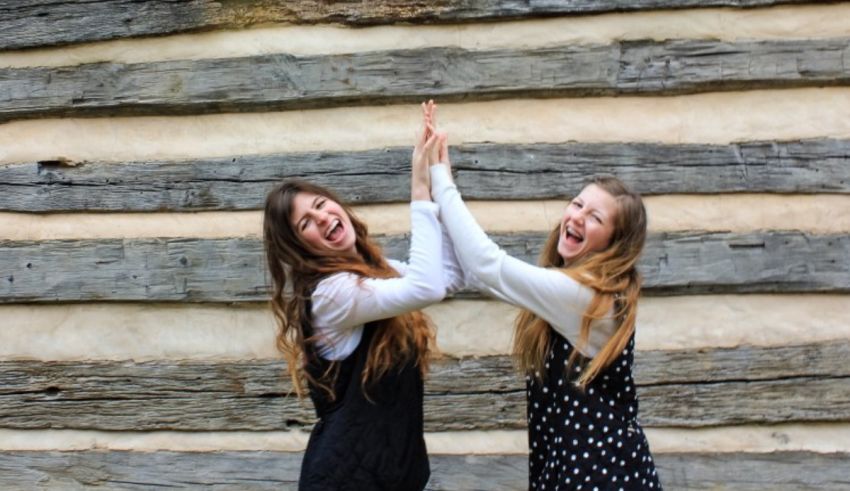 Two girls giving each other high fives in front of a log cabin.