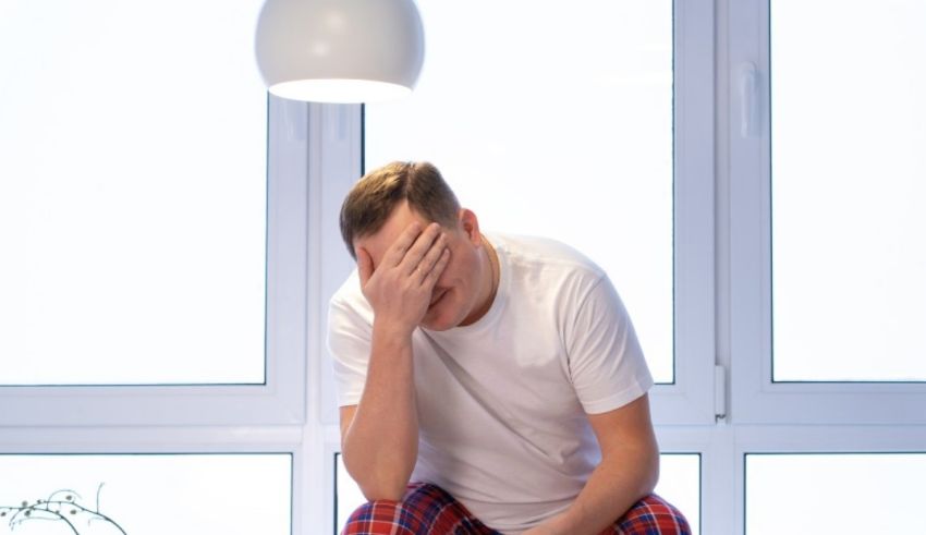 A man in pajamas sitting on the floor in front of a window.