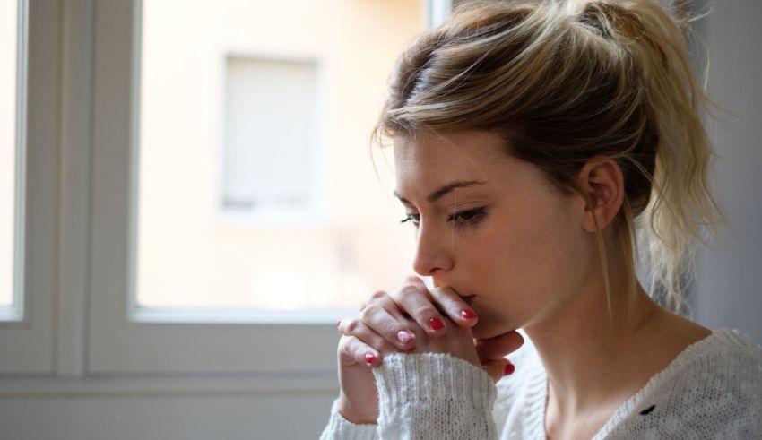 A woman is sitting in front of a window with her hands on her chin.