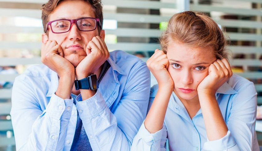 A man and a woman sitting in an office with their hands on their heads.