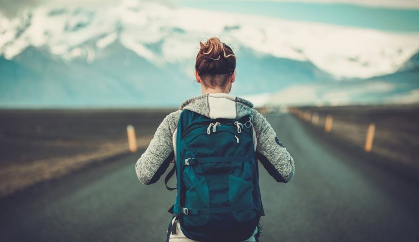 A woman with a backpack walking down a road with mountains in the background.