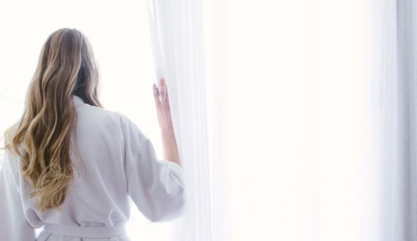 A woman in a white bathrobe looking out the window.