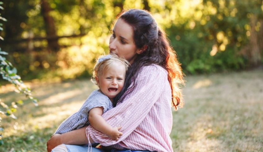 A woman is holding a crying baby in the grass.