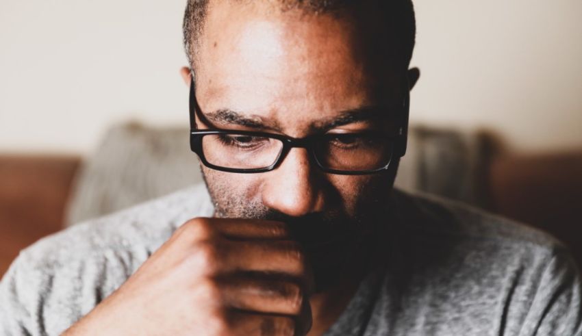 A man with glasses is holding his hand to his face.