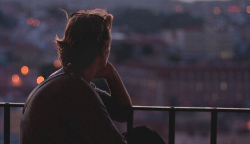 A woman sitting on a balcony overlooking a city at night.