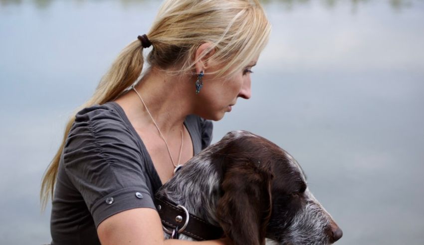 A woman holding a dog near a body of water.