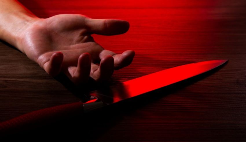 A person's hand with a knife on top of a wooden table.