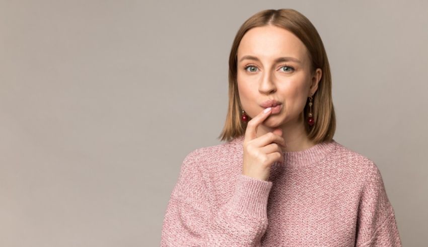 A young woman with a pink sweater and a finger in her mouth.