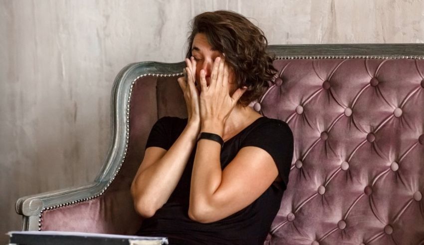 A woman sitting on a couch with her hands covering her face.