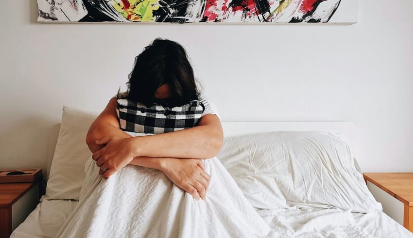 A woman is sitting in bed with her arms wrapped around her.