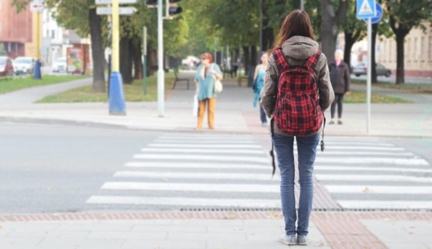 A woman with a backpack is crossing a street.